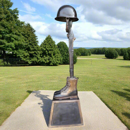 WWII War Memorial Battle Cross with boots, old-era rifle, and helmet - Sitting outside, on a sunny day, in a green grassy landscape. 