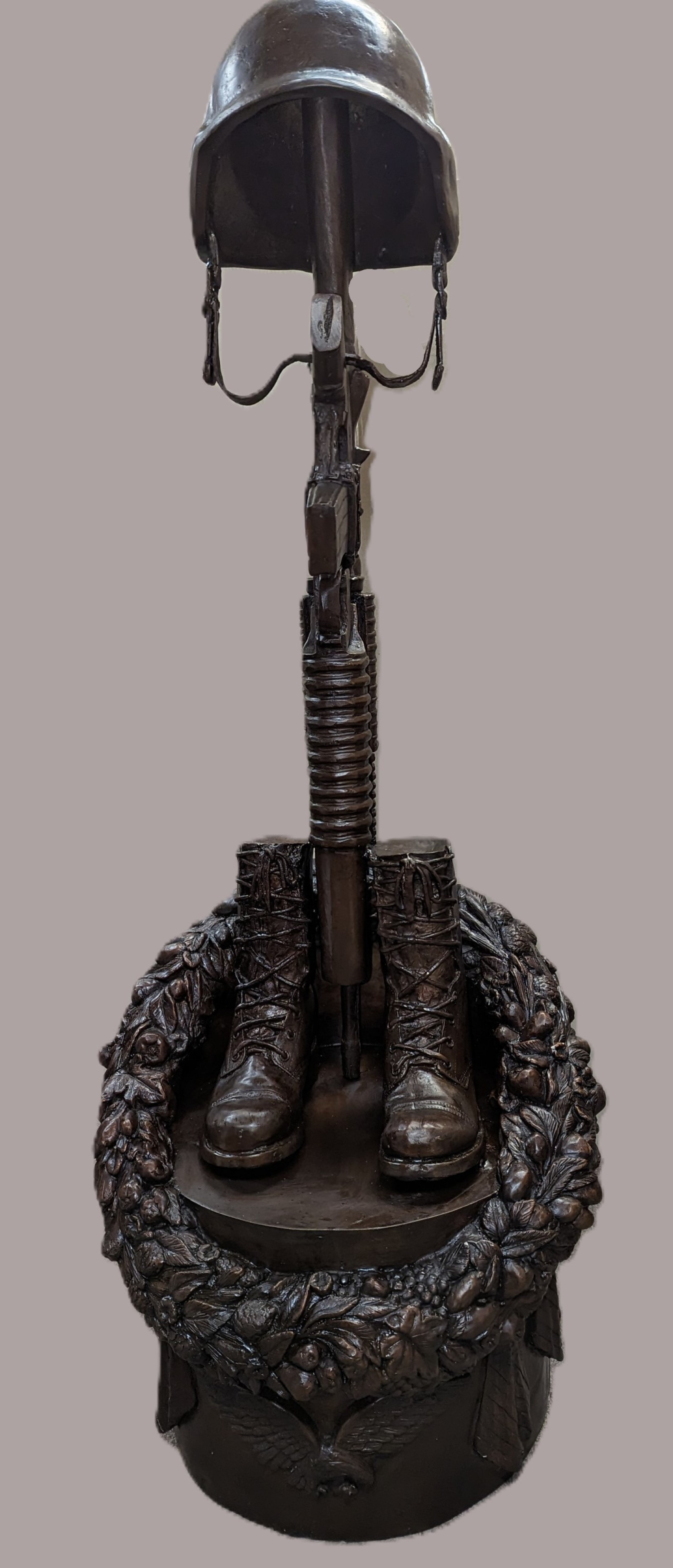 Bronze sculpture of a military figure with helmet, boots, and rifle on a gray background