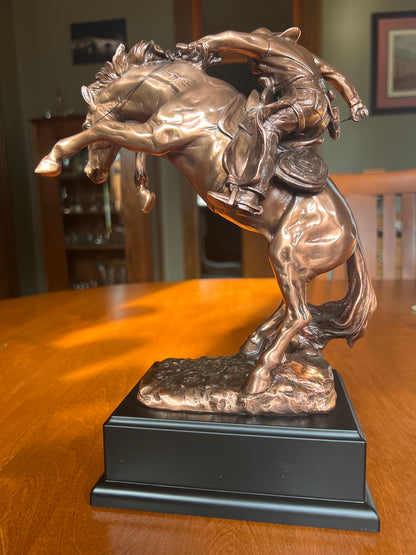 Western cowboy riding a rearing bronco sculpture in bronze finish