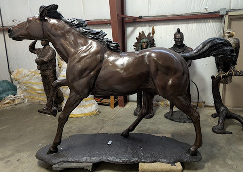 Bronze statue of a horse in a dynamic pose with figures in the background.