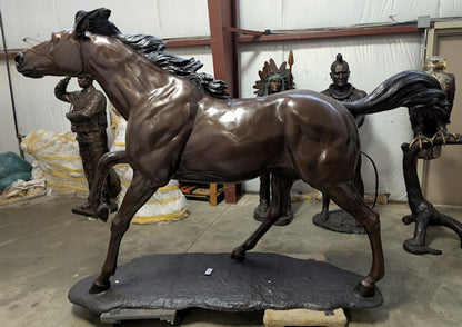 Bronze statue of a horse in a dynamic pose with figures in the background.