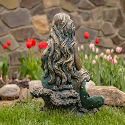 Back view of mermaid garden statue showing flowing hair, curved tail, and sculpted rock details