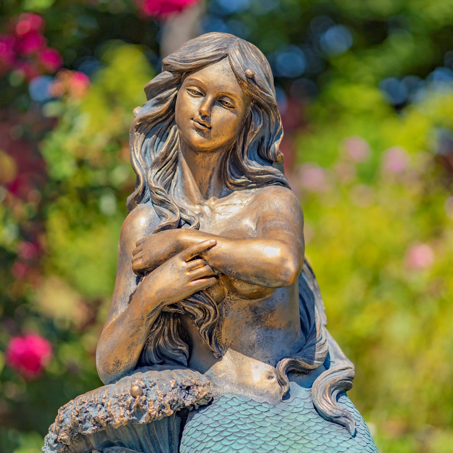 Antique bronze mermaid garden statue shown from the front with teal scaled tail and rocky waves