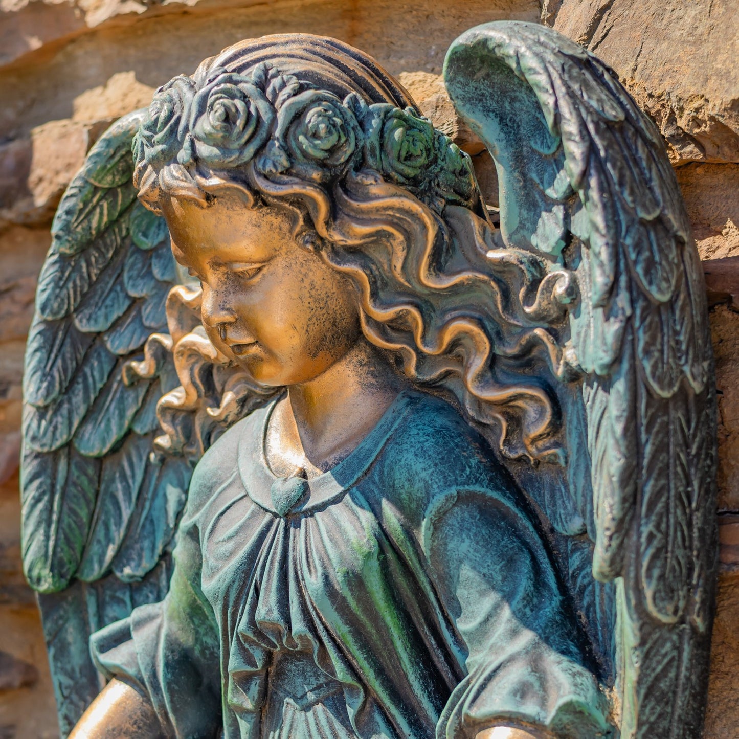 Bronze angel statue with floral headpiece against a stone wall